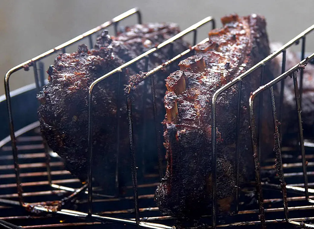 Slabs of ribs standing in rib racks over a grill, crusted dark